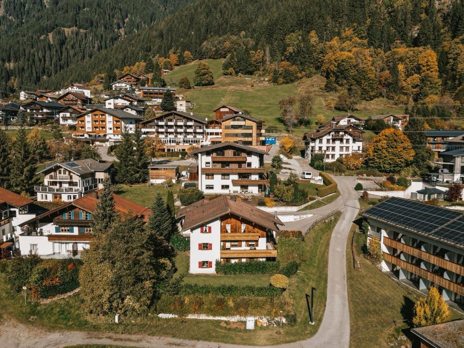 Weitläufige Luftaufnahme eines charmanten Bergdorfes, eingebettet in eine grüne Herbstlandschaft.