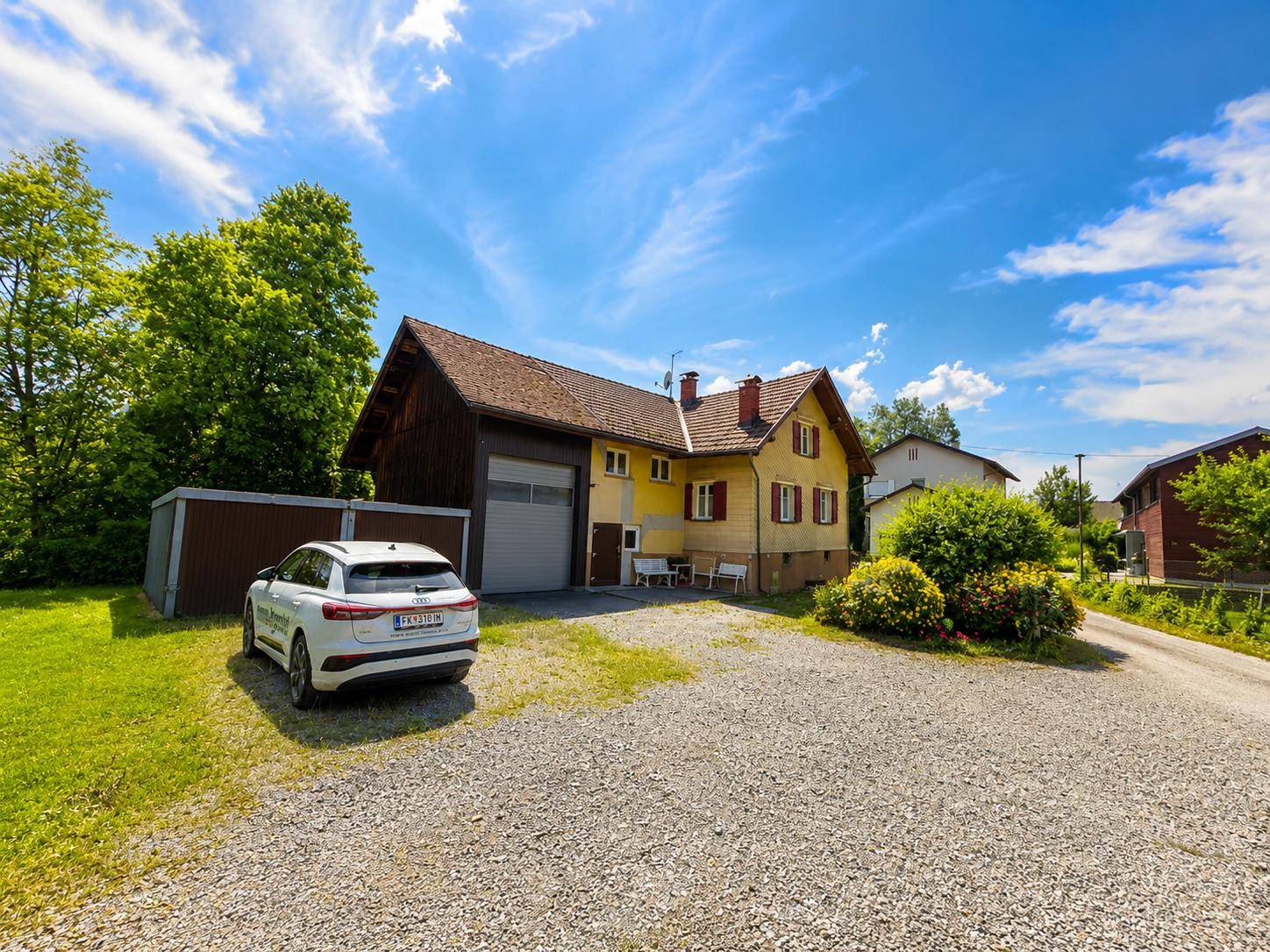 Traditionelles Einfamilienhaus mit gelber Fassade, Garage und Schotterparkplatz im Grünen.