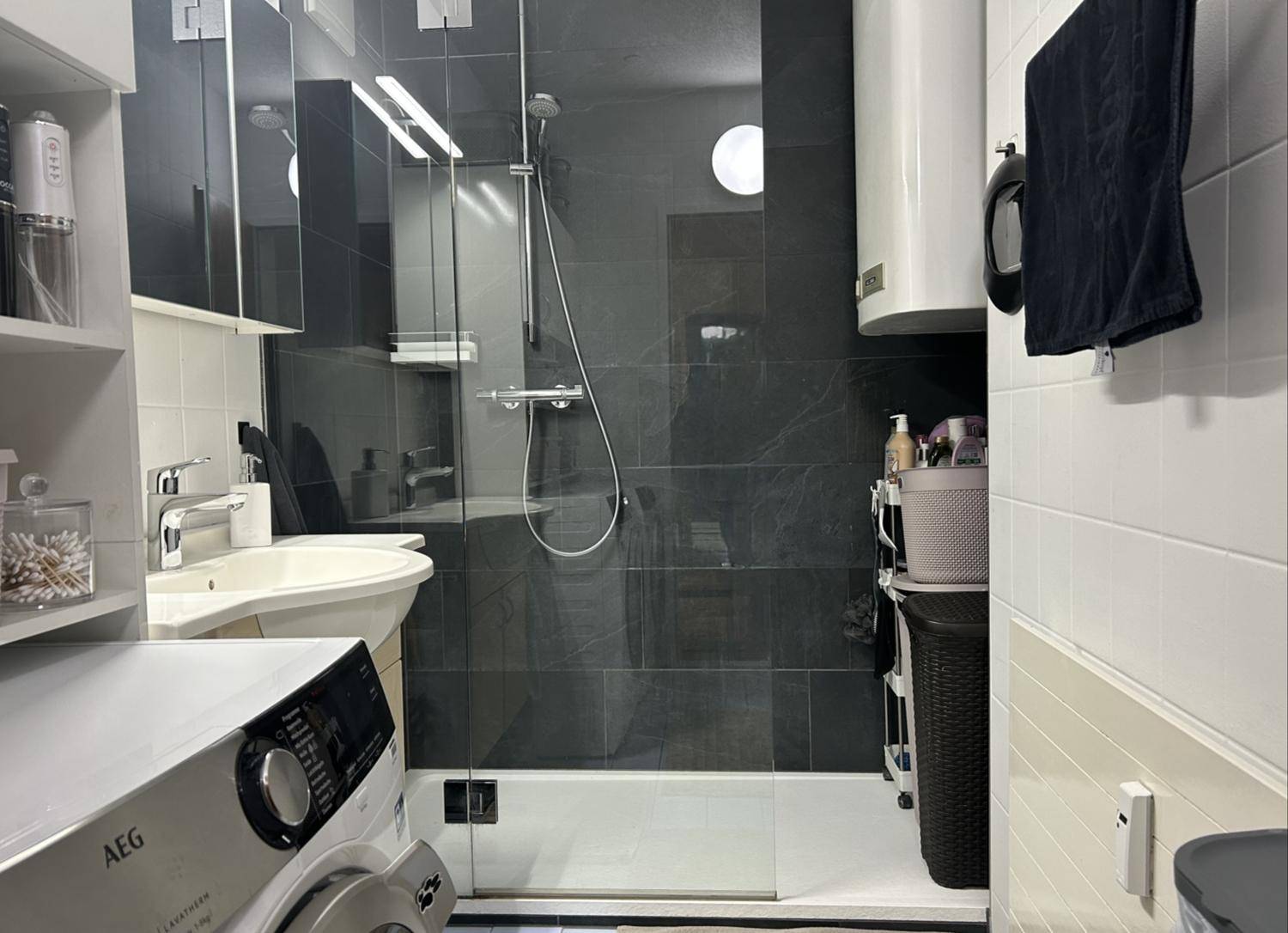 Modernes Badezimmer mit ebenerdiger Dusche, dunklen Fliesen und integrierter Waschmaschine.