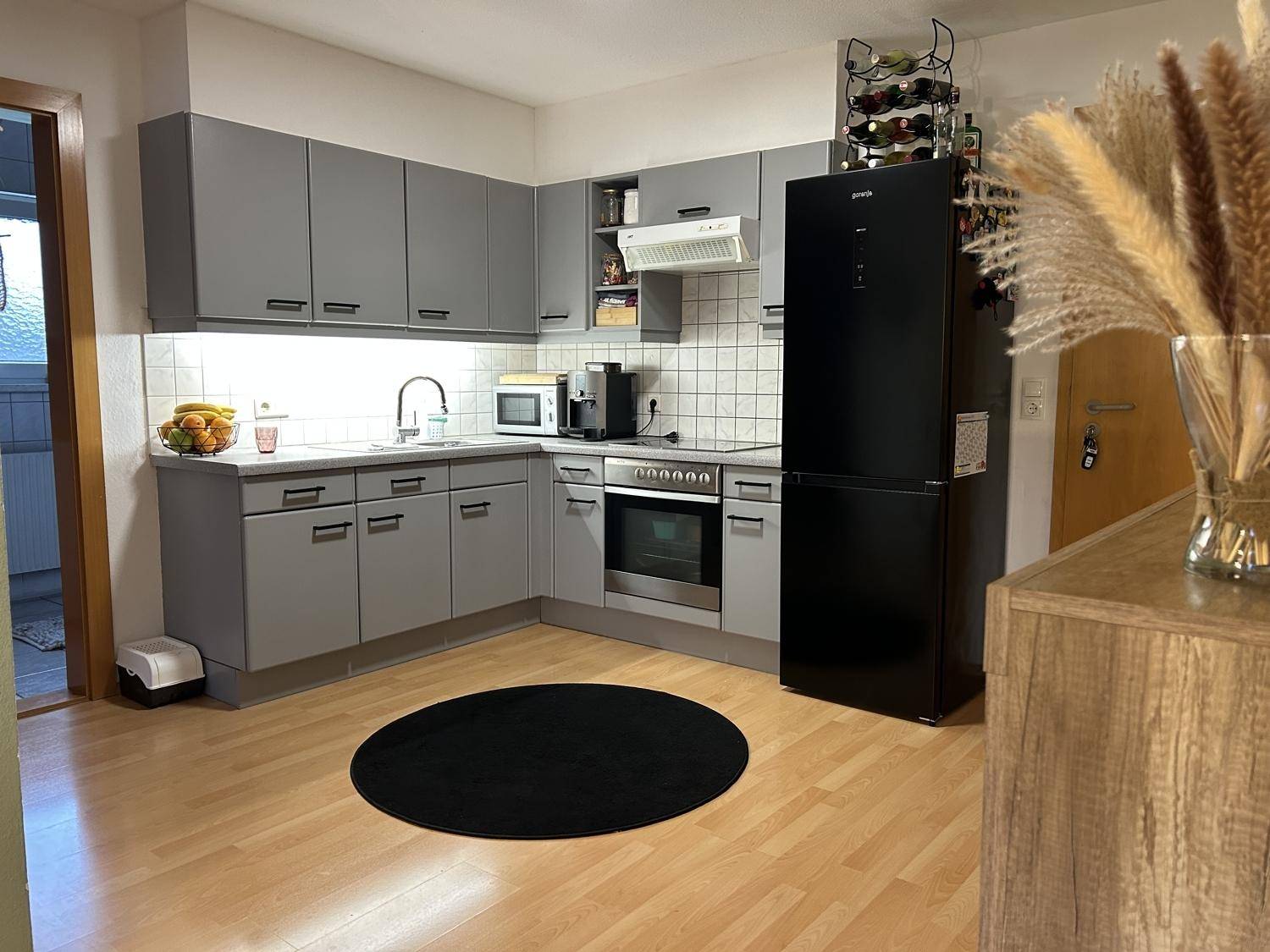 Moderne Küche mit grauen Schränken, schwarzem Kühlschrank und Induktionskochfeld auf hellem Holzboden.