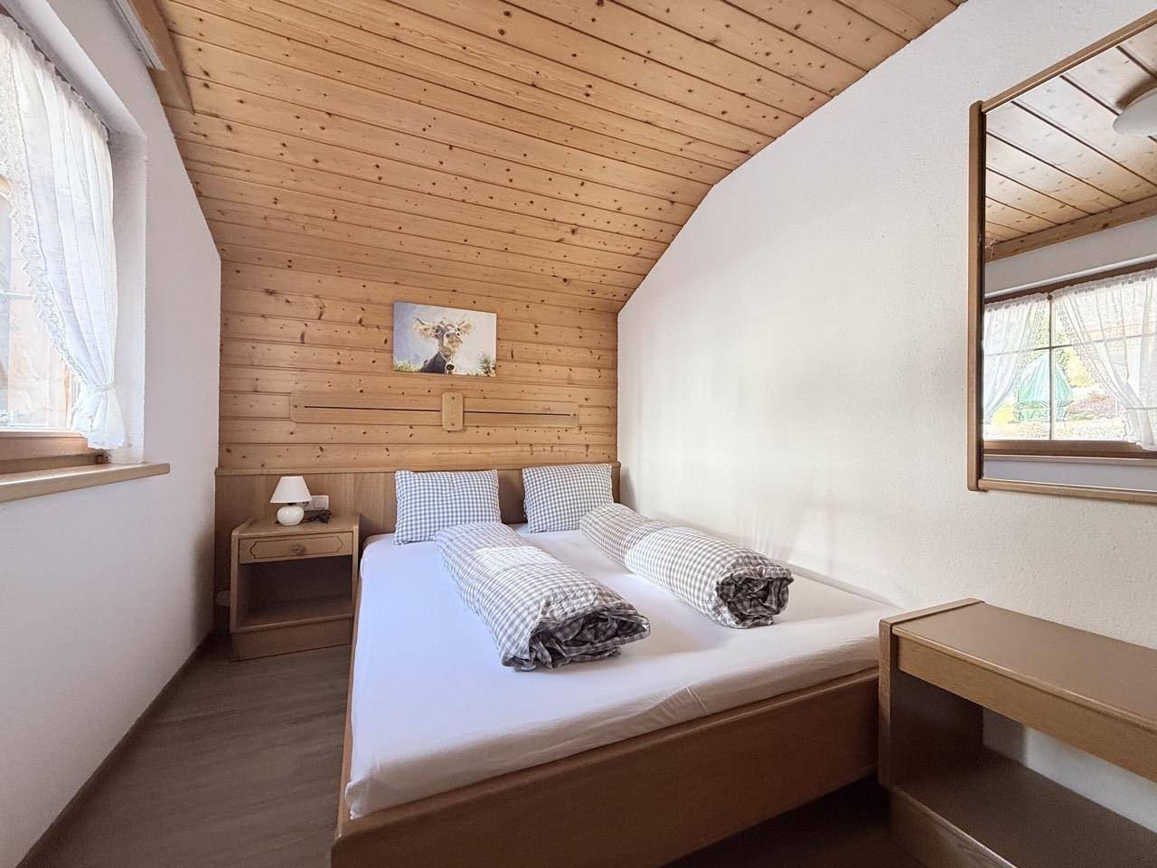 Gemütliches Schlafzimmer mit Holzverkleidung, Doppelbett und Fenster mit Blick nach draußen.