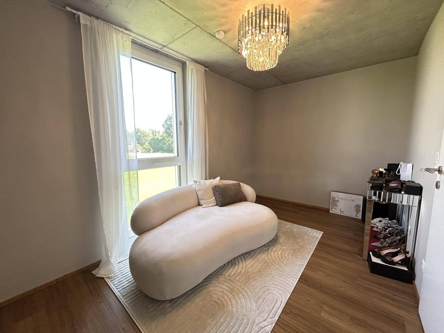 Helles Zimmer mit modernem Sofa, großem Fenster und Blick ins Grüne.