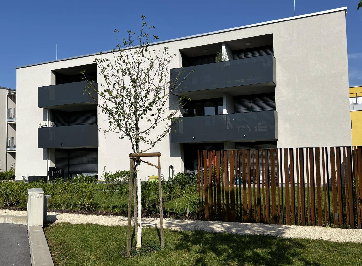 Moderne Wohngebäude mit Balkonen und gepflegten Grünflächen unter blauem Himmel.