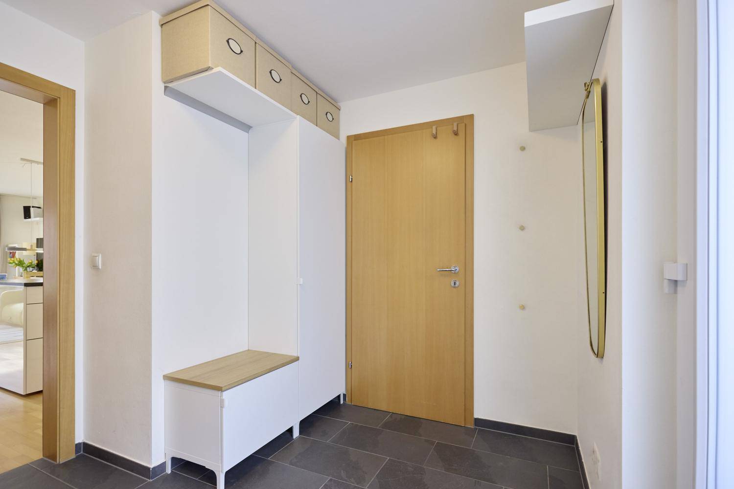 Eingangsbereich mit Garderobe, Spiegel und dunklen Bodenfliesen.