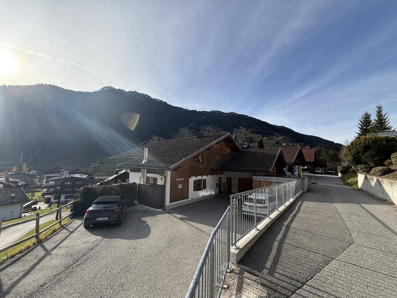 Haus mit Zufahrt und Parkplatz, umgeben von grünen Hängen und Bergen.