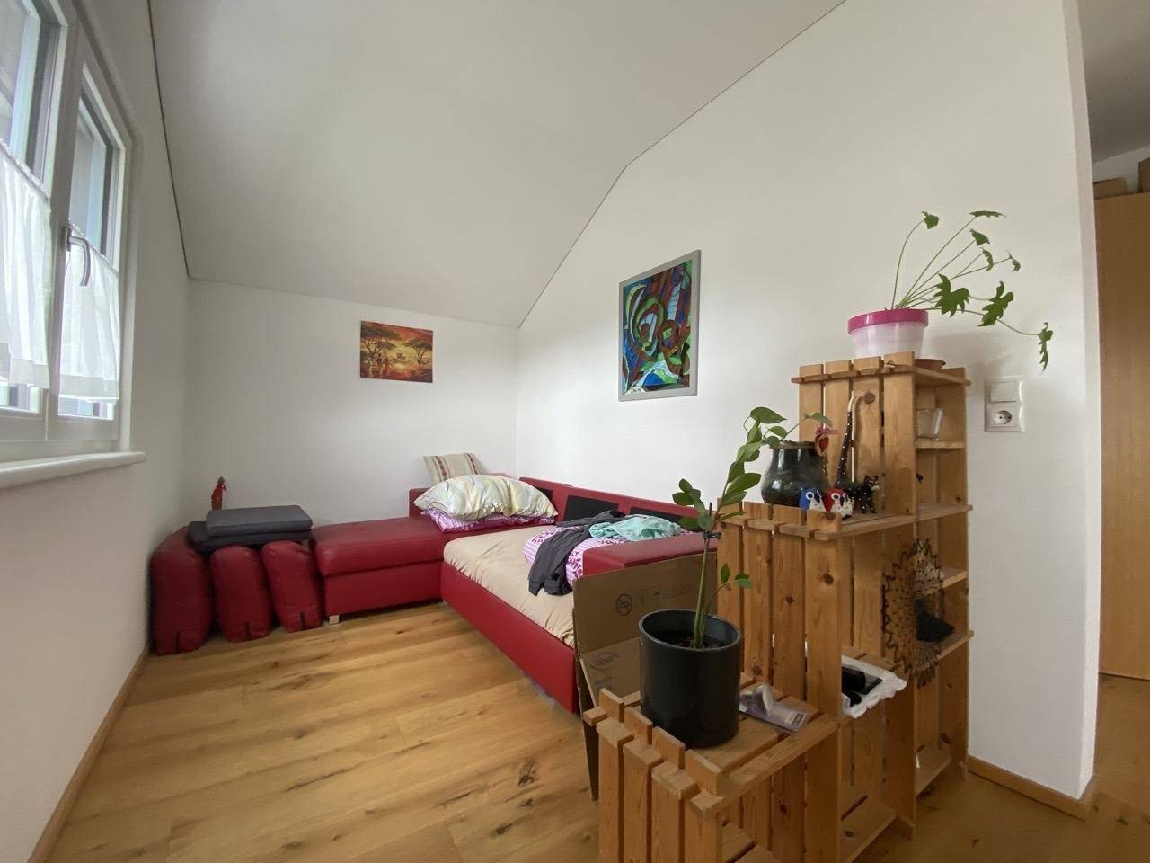 Helles Schlafzimmer mit Dachschräge, Holzboden und farbenfroher Dekoration.
