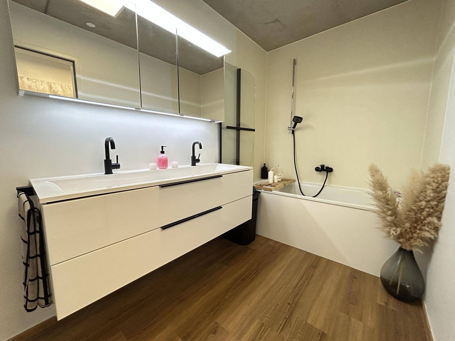 Modernes Badezimmer mit Doppelwaschbecken, Badewanne und eleganten schwarzen Armaturen.
