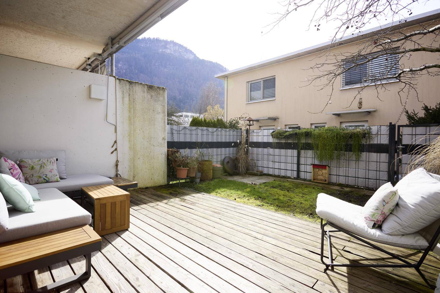 Sonniger Terrassenbereich mit Holzdeck, Gartenmöbeln und Bergblick.