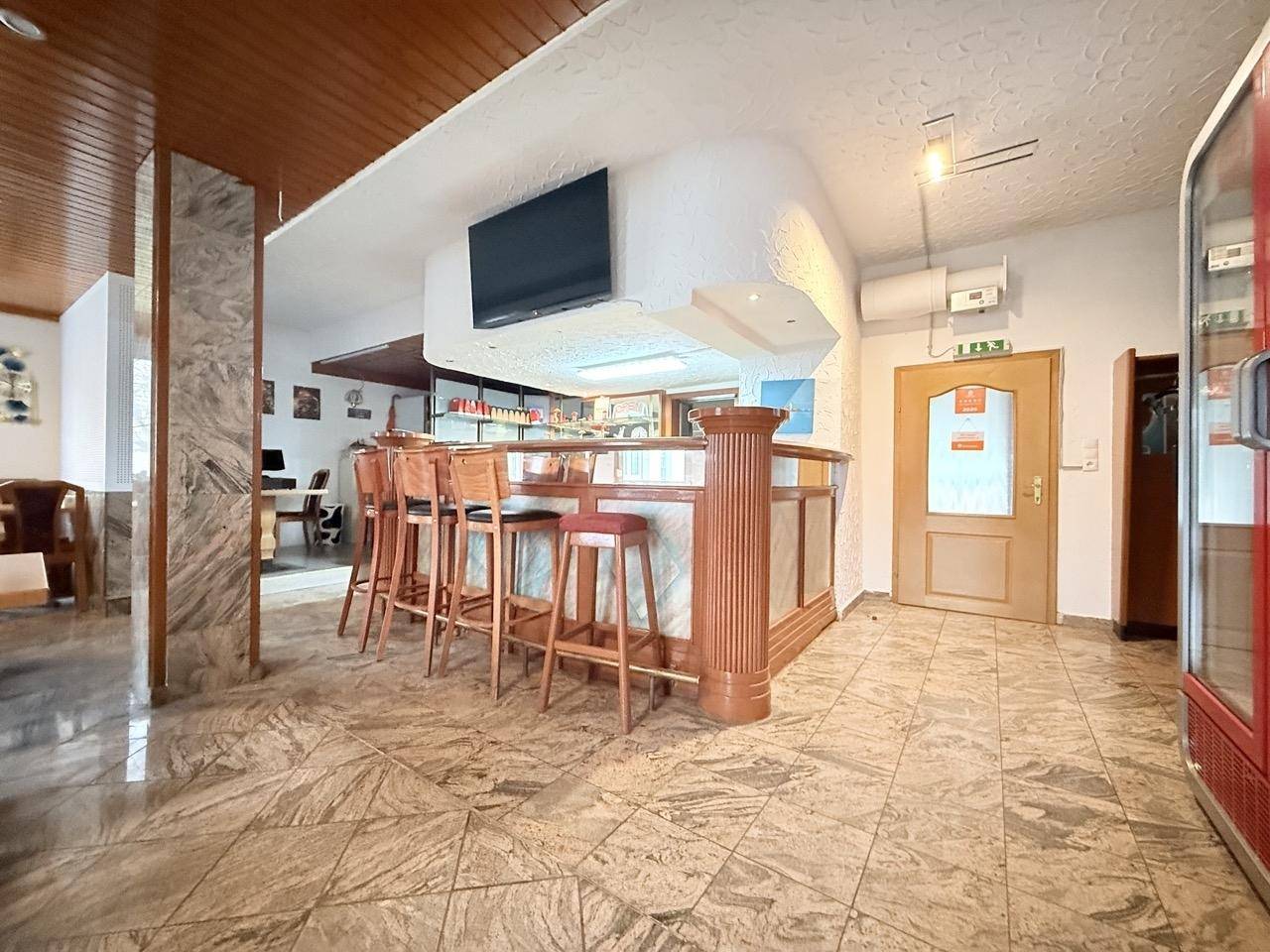 Bar mit Holzsäule, Barhockern und einem Fernseher in einem gefliesten Raum.