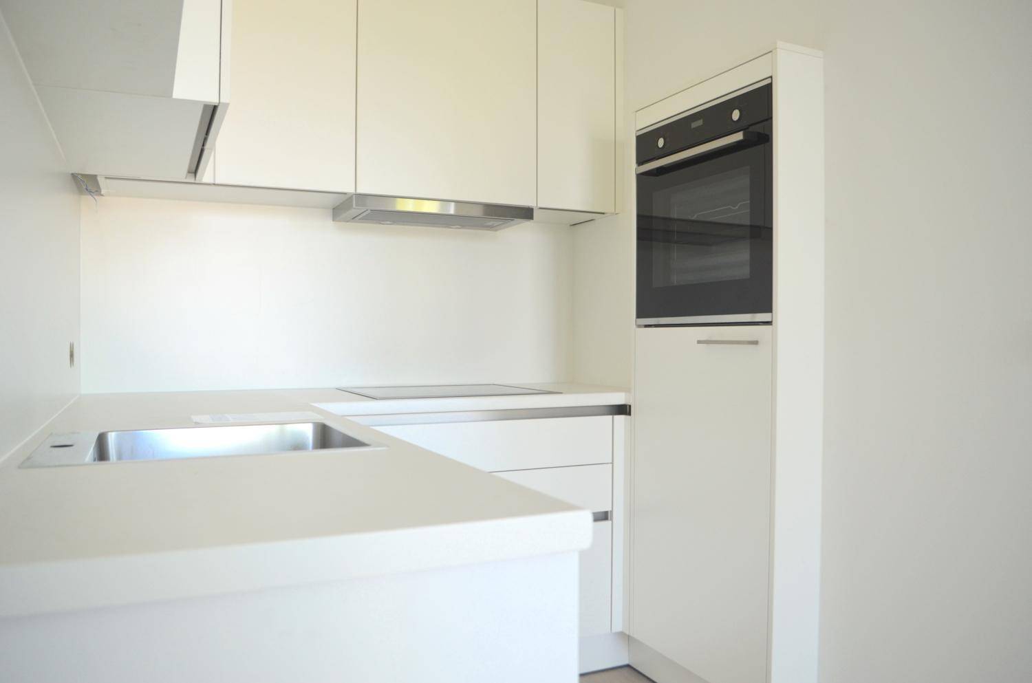 Moderne, helle Einbauküche in Weiß mit integriertem Backofen und Induktionskochfeld.