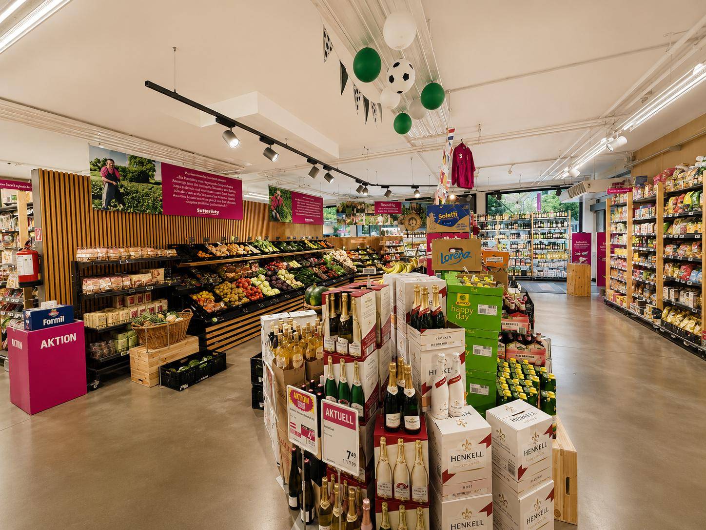Frischeabteilung eines Supermarktes mit Obst- und Gemüseständen sowie speziellen Getränkeauslagen und Dekorationen.