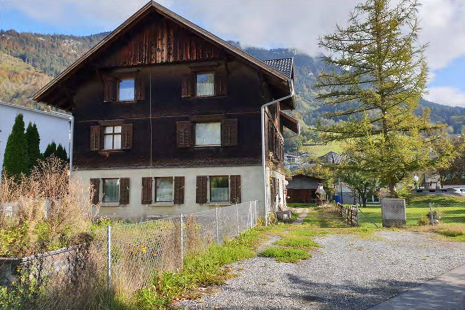 Traditionelles Holzhaus mit Satteldach und brauner Fassade, umgeben von Bergen und Natur.