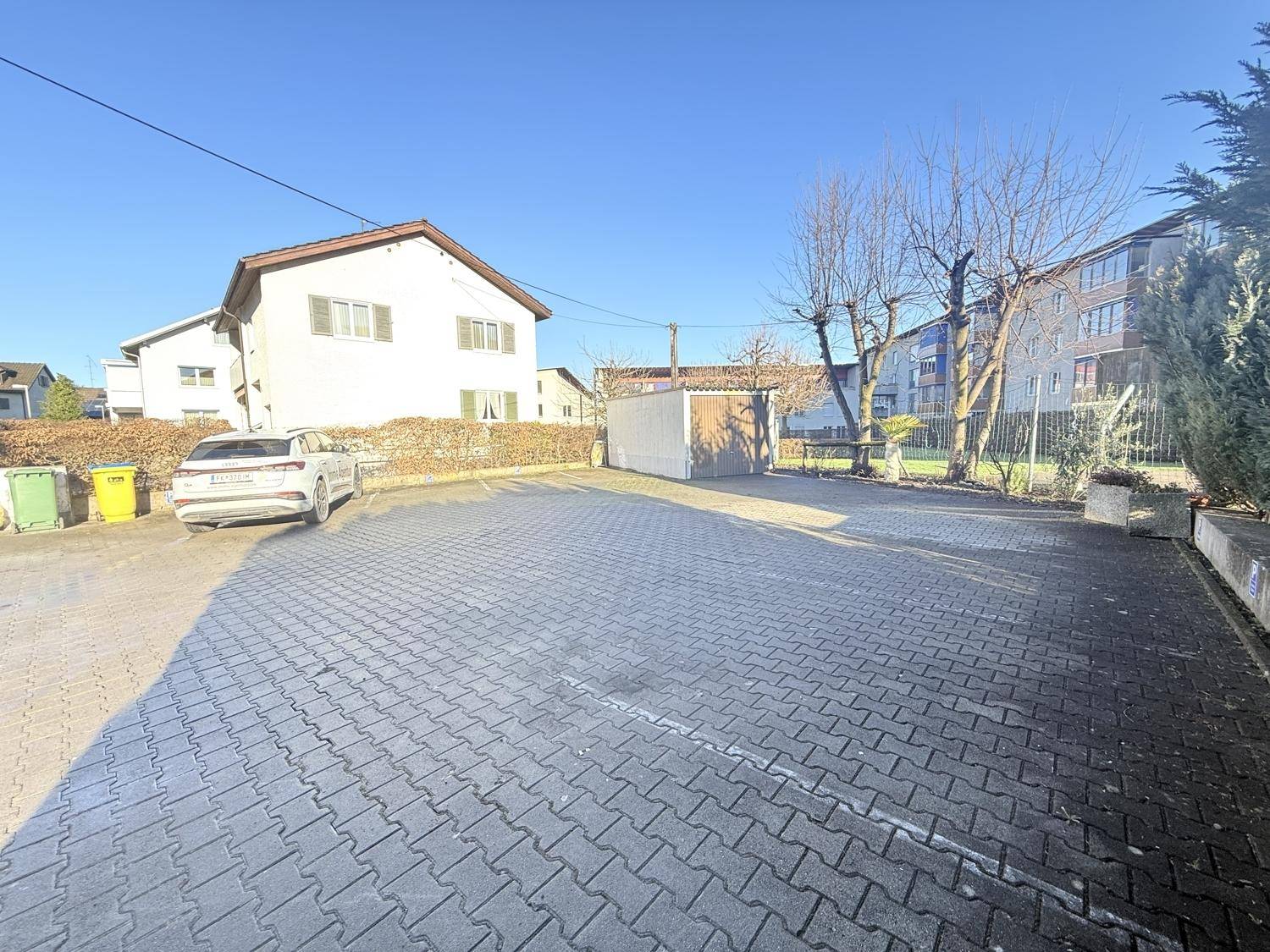Großer gepflasterter Parkplatz mit einem Auto und umgebender Vegetation.