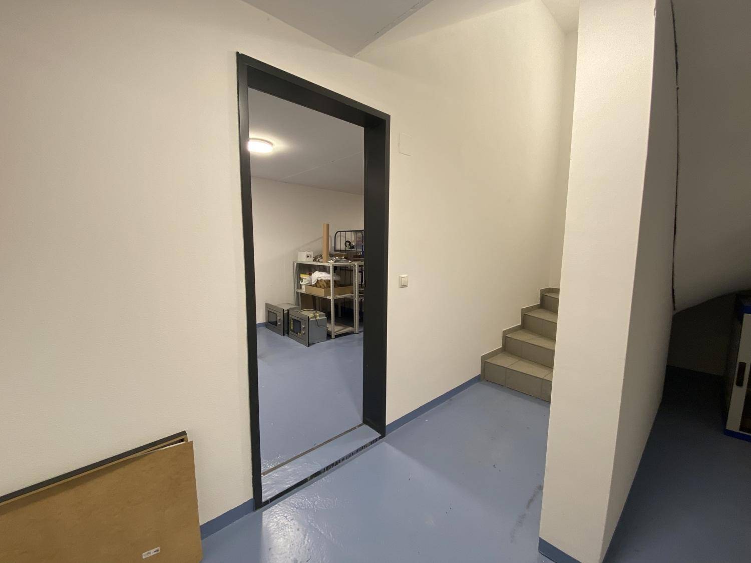 Geräumiger Flur mit Treppe und Blick in einen angrenzenden Raum, der als Lager dient.