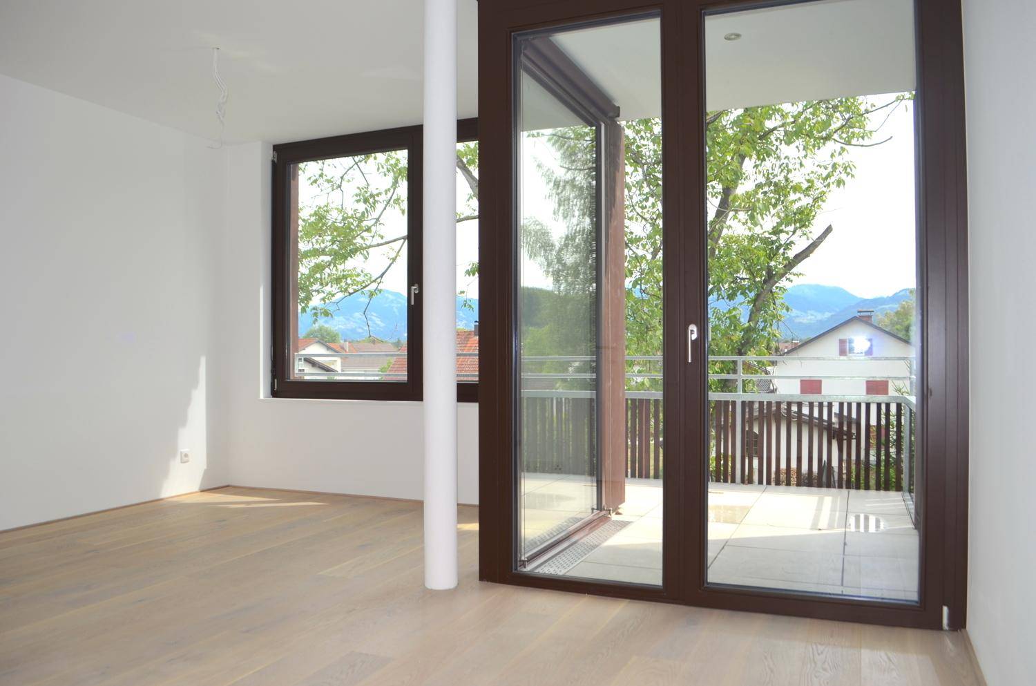 Heller Wohnraum mit Holzboden, großen Fenstern und Zugang zu einem Balkon mit Bergblick.