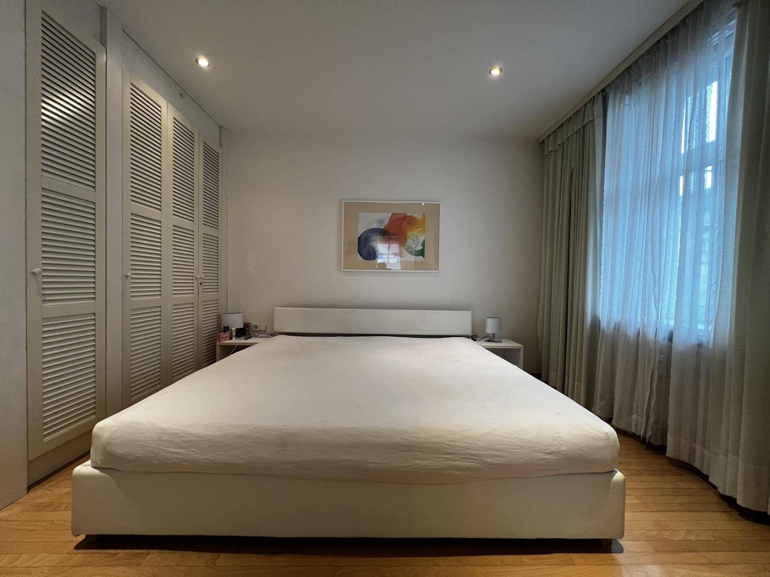 Schlafzimmer mit großem Bett, praktischen Einbauschränken und Fenster mit Vorhängen für angenehme Nächte.
