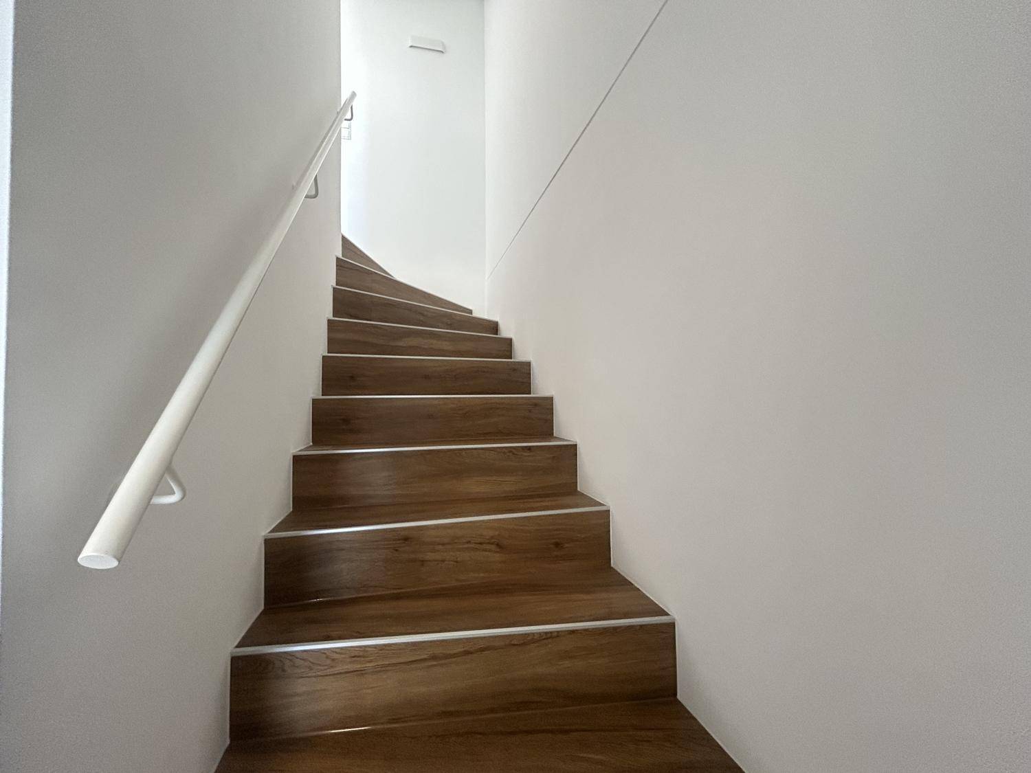 Funktionale Holztreppe mit weißem Geländer und hellen Wänden, die in die obere Etage führt.
