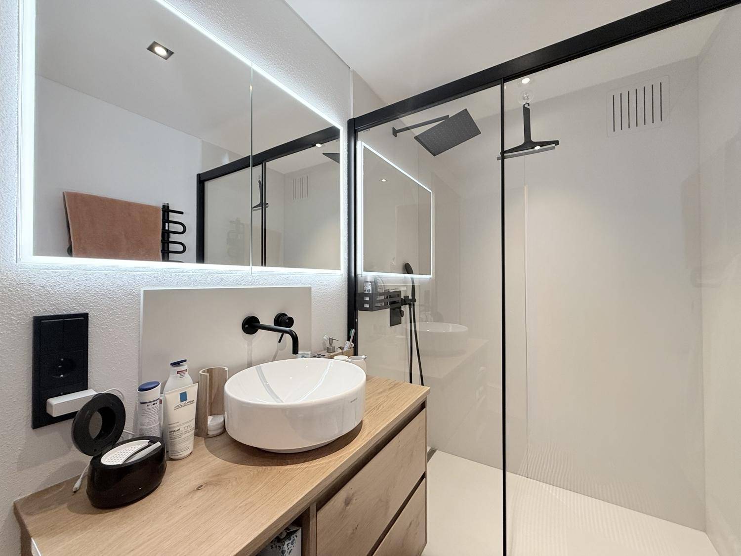 Modernes Badezimmer mit elegantem Einzelwaschbecken, beleuchtetem Spiegelschrank und begehbarer Dusche.