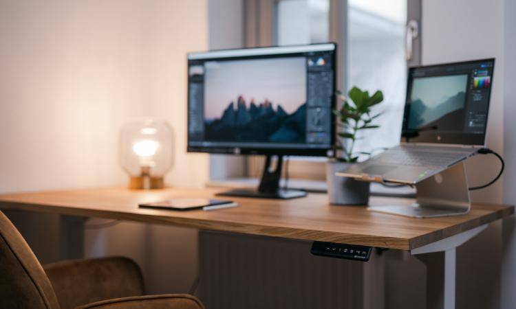 Modern eingerichteter Arbeitsplatz mit Stehschreibtisch, Monitor und Laptop vor einem Fenster.