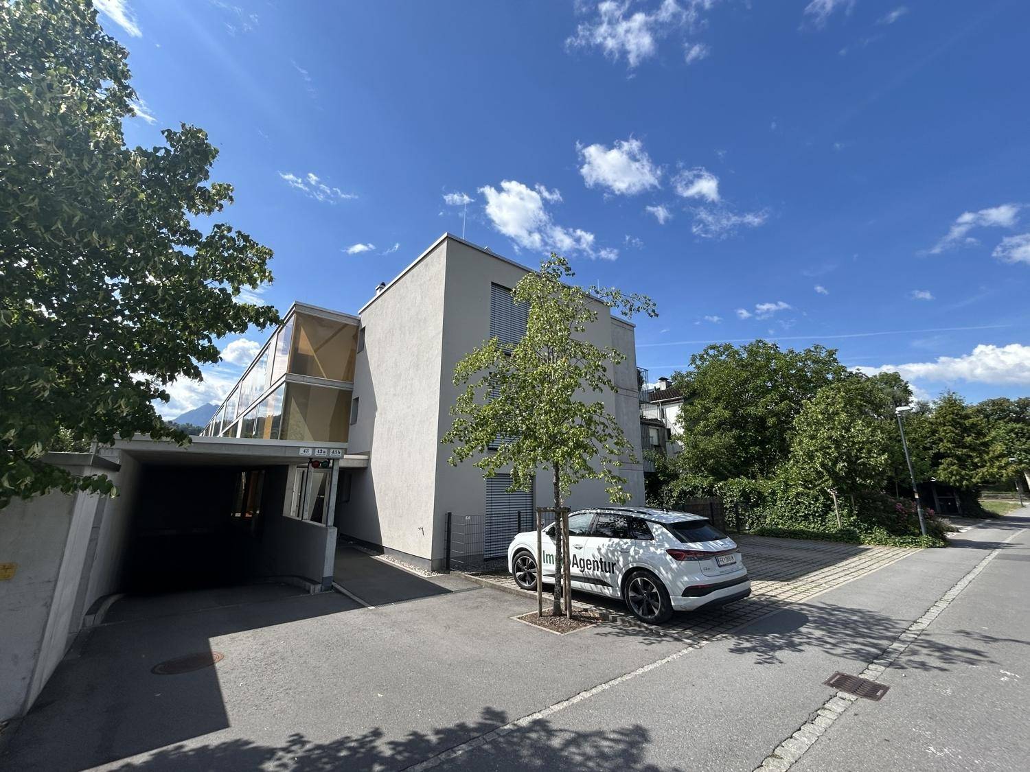 Modernes Wohngebäude mit schlichter Fassade, umgeben von Bäumen unter strahlend blauem Himmel.