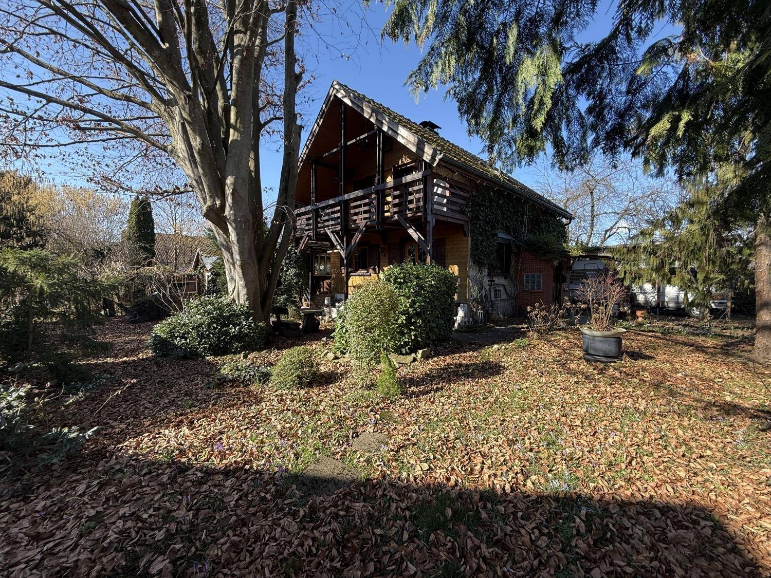 Holzhaus im Chalet-Stil mit Balkon und großem Garten, umgeben von Bäumen und Herbstlaub.