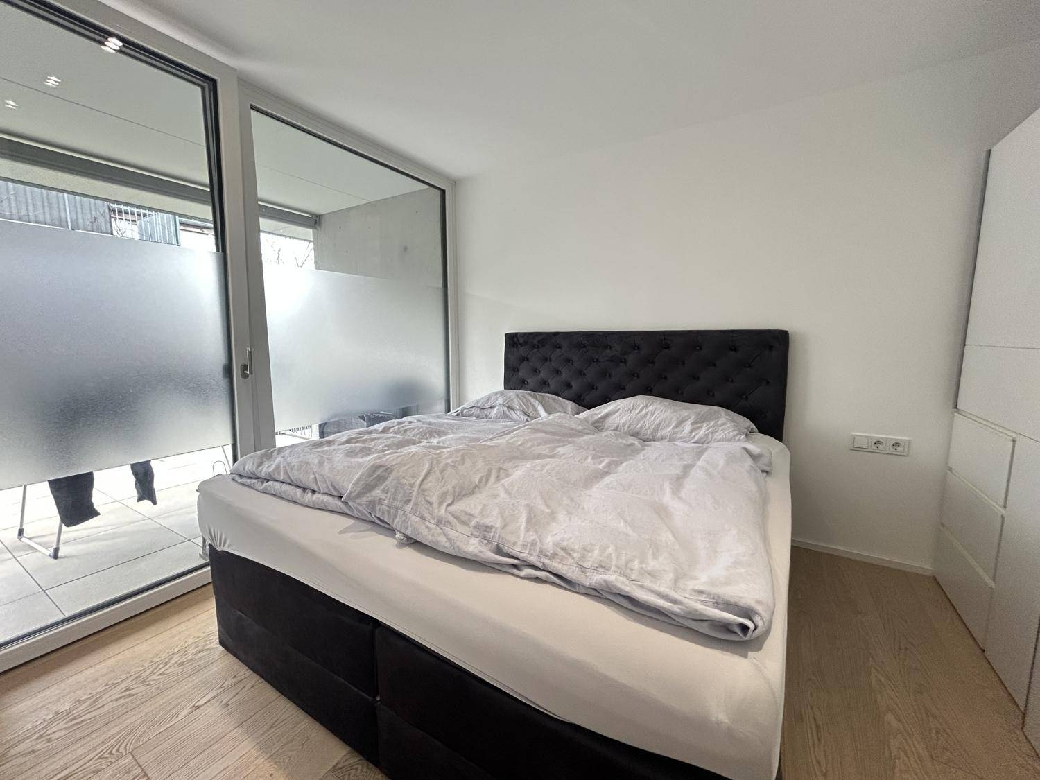 Schlafzimmer mit großem Bett, Holzboden und Zugang zu einem Außenbereich.