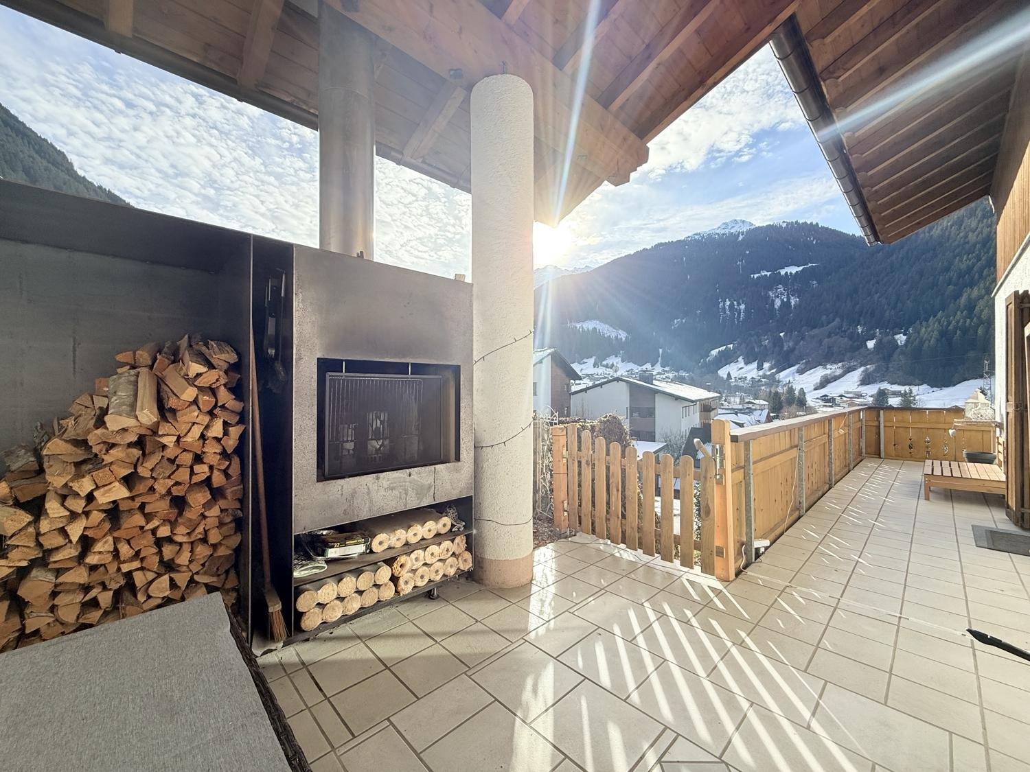 Sonnige Terrasse mit integriertem Grillkamin, Holzstapel und herrlichem Bergblick.