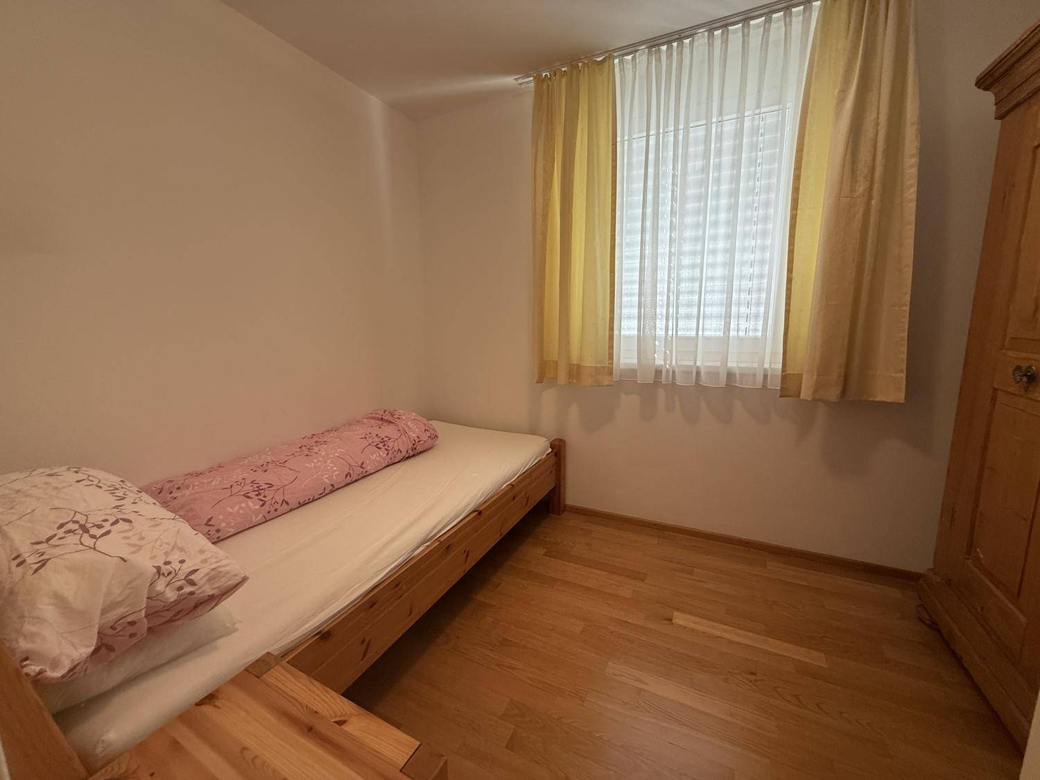 Gemütliches Schlafzimmer mit Holzboden, Einzelbett und Holzschrank, gut beleuchtet.