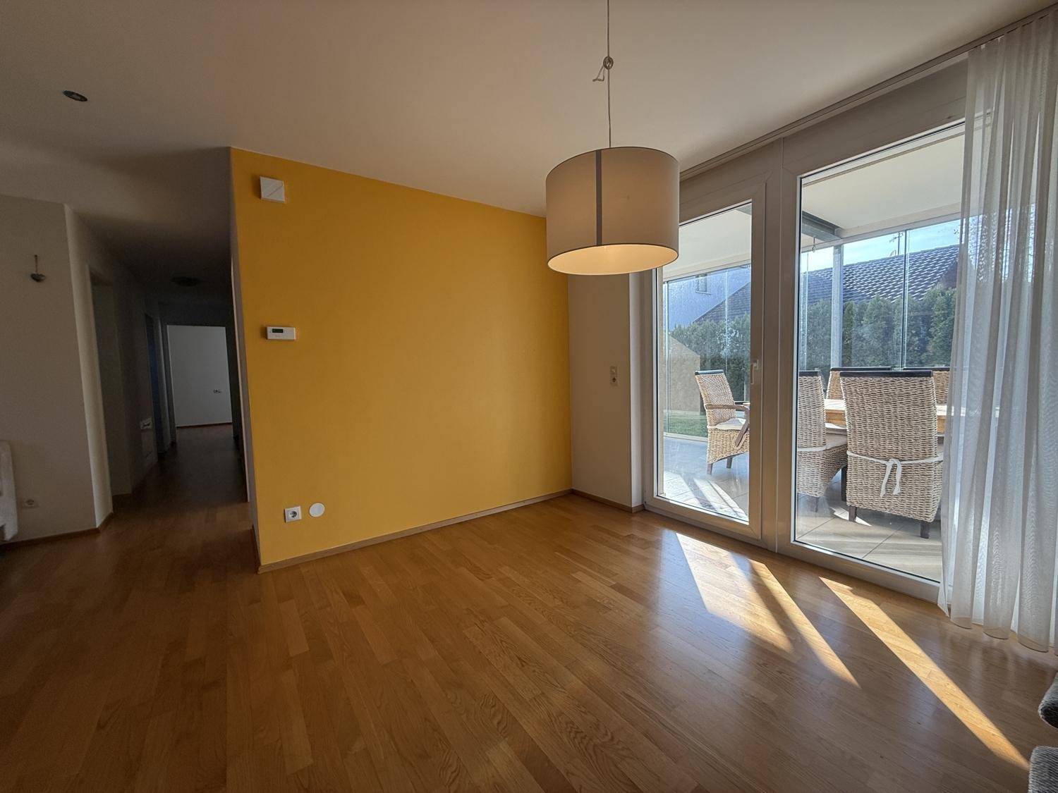 Helles Wohnzimmer mit Holzboden und Zugang zu einer verglasten Terrasse mit Sitzgelegenheiten.