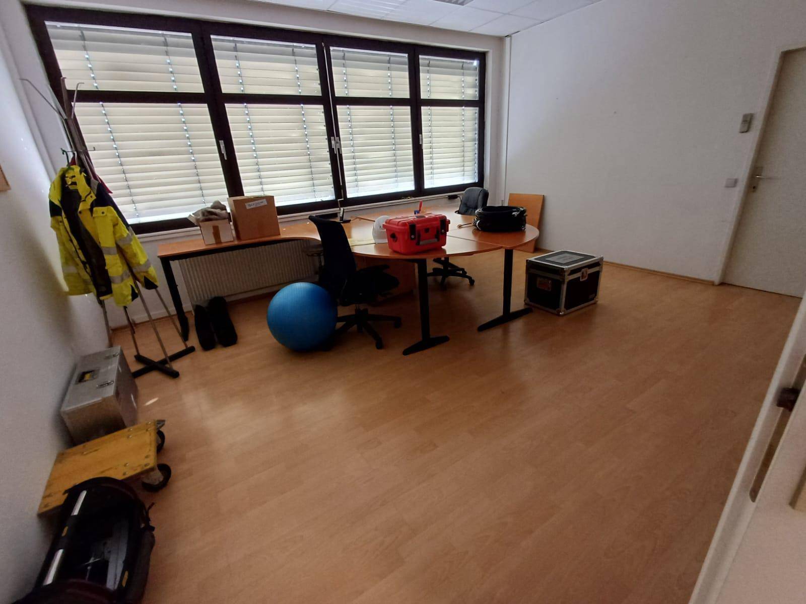 Geräumiger Büroraum mit Schreibtisch, Bürostuhl, einem blauen Gymnastikball und großen Fenstern.