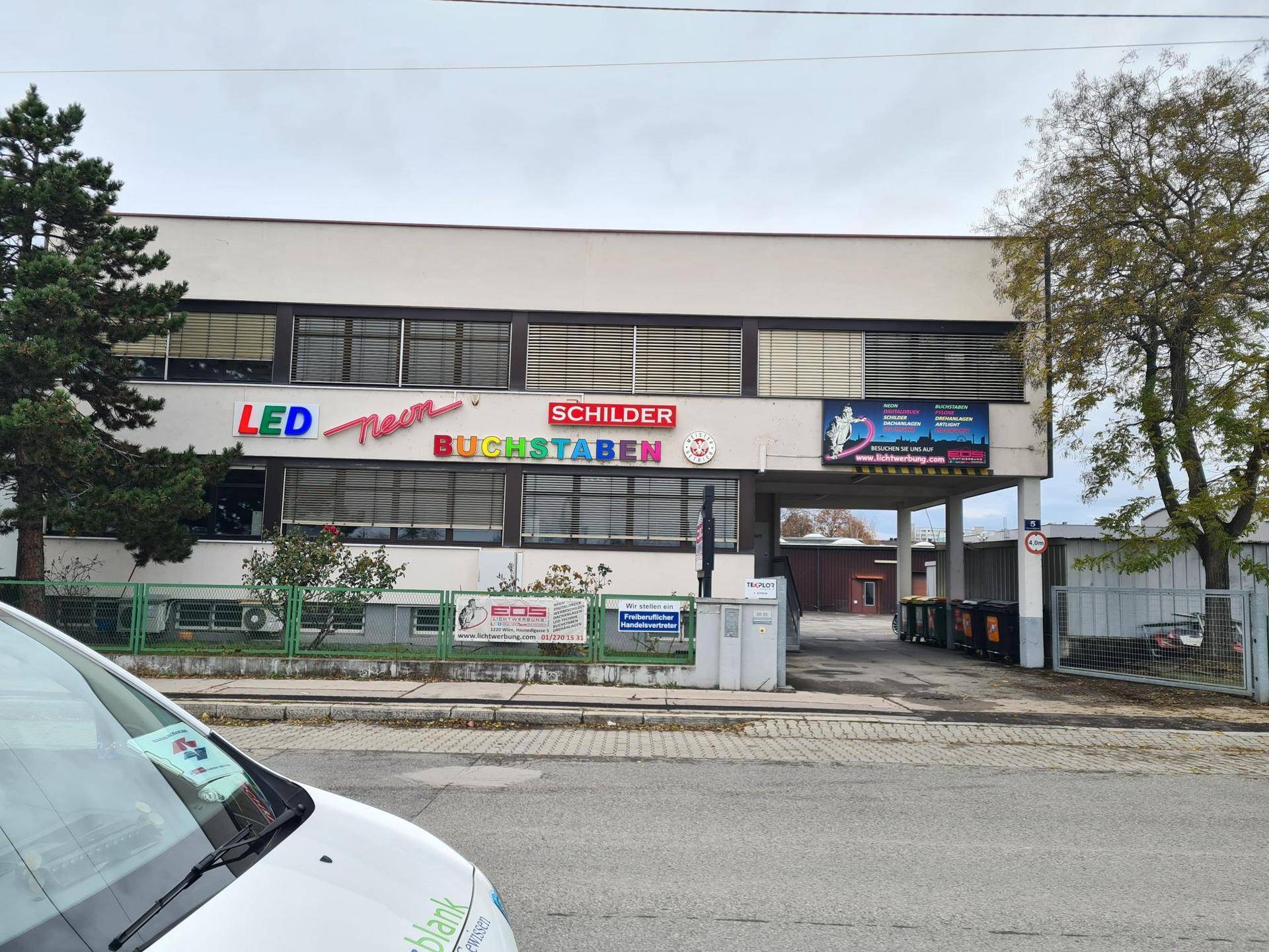 Gewerbegebäude mit LED-Neon-Schildern und einem teilweise sichtbaren Fahrzeug im Vordergrund.
