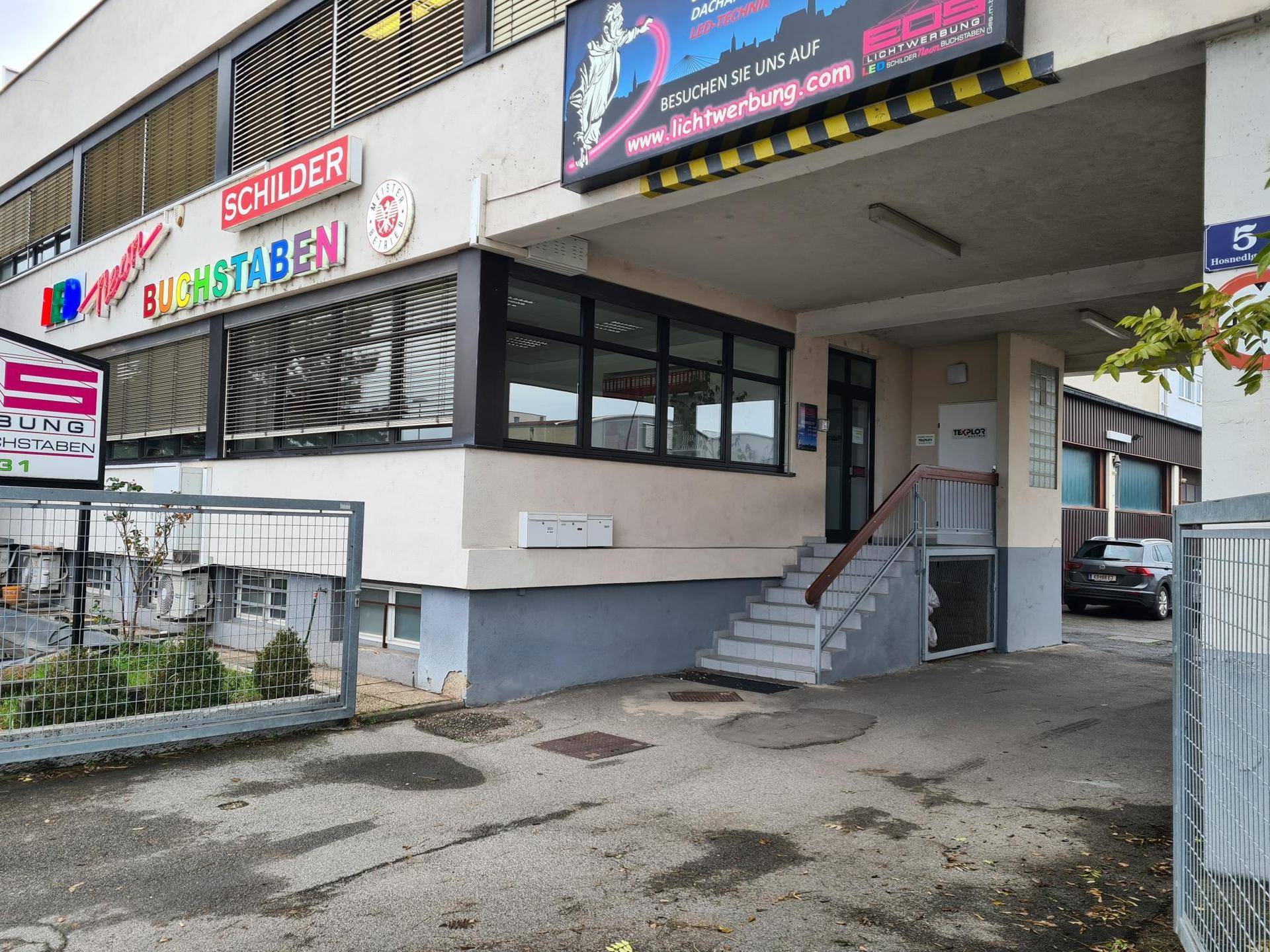 Nahaufnahme des Eingangs zum Gewerbegebäude mit Treppenaufgang und überdachtem Zugangsbereich.