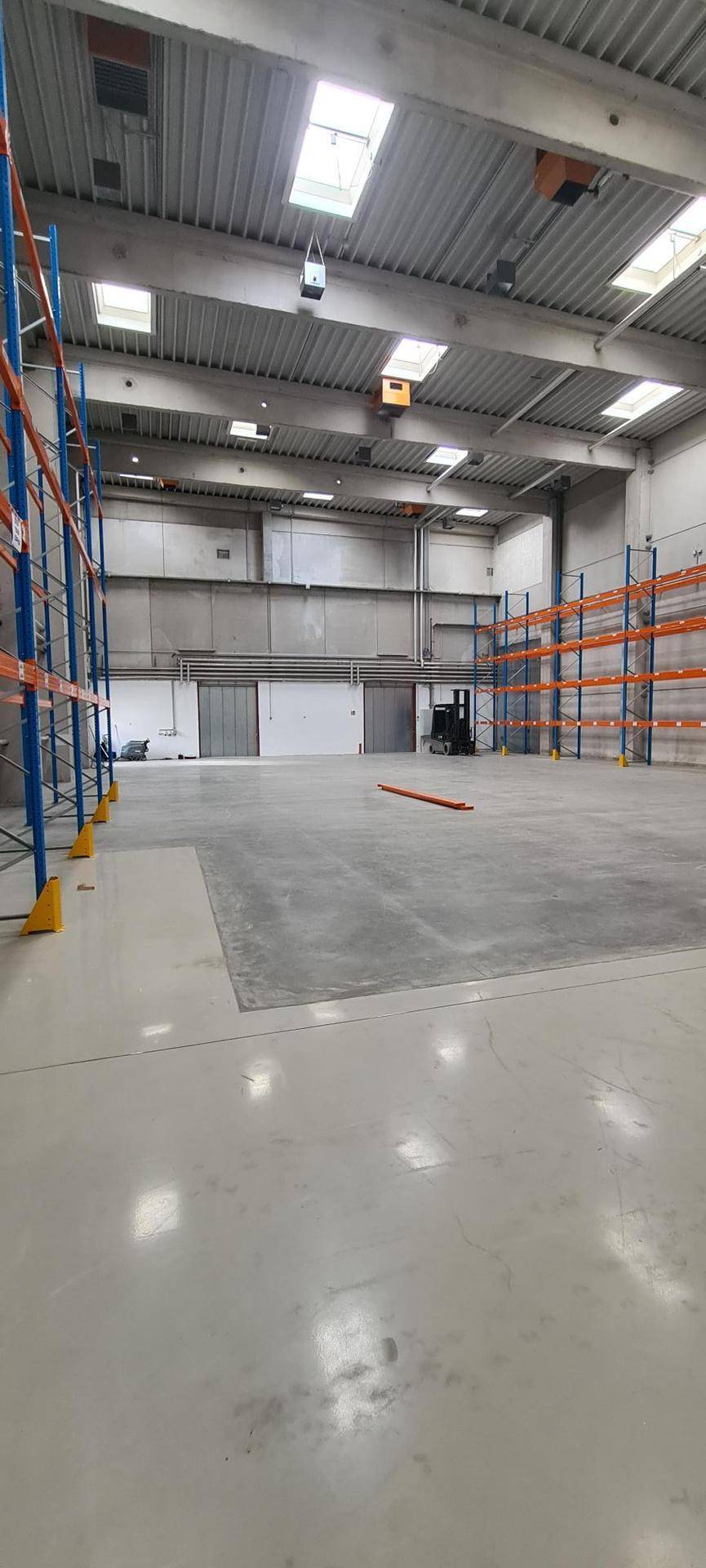 Leere Lagerhalle mit hohen Decken, Betonboden und installierten, aber unbestückten Regalsystemen.