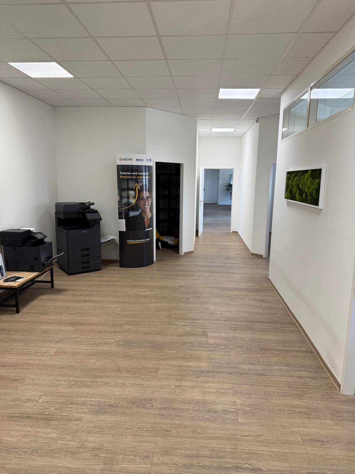 Heller Bürogang mit Laminatboden, weißen Wänden und einem Druckerbereich.