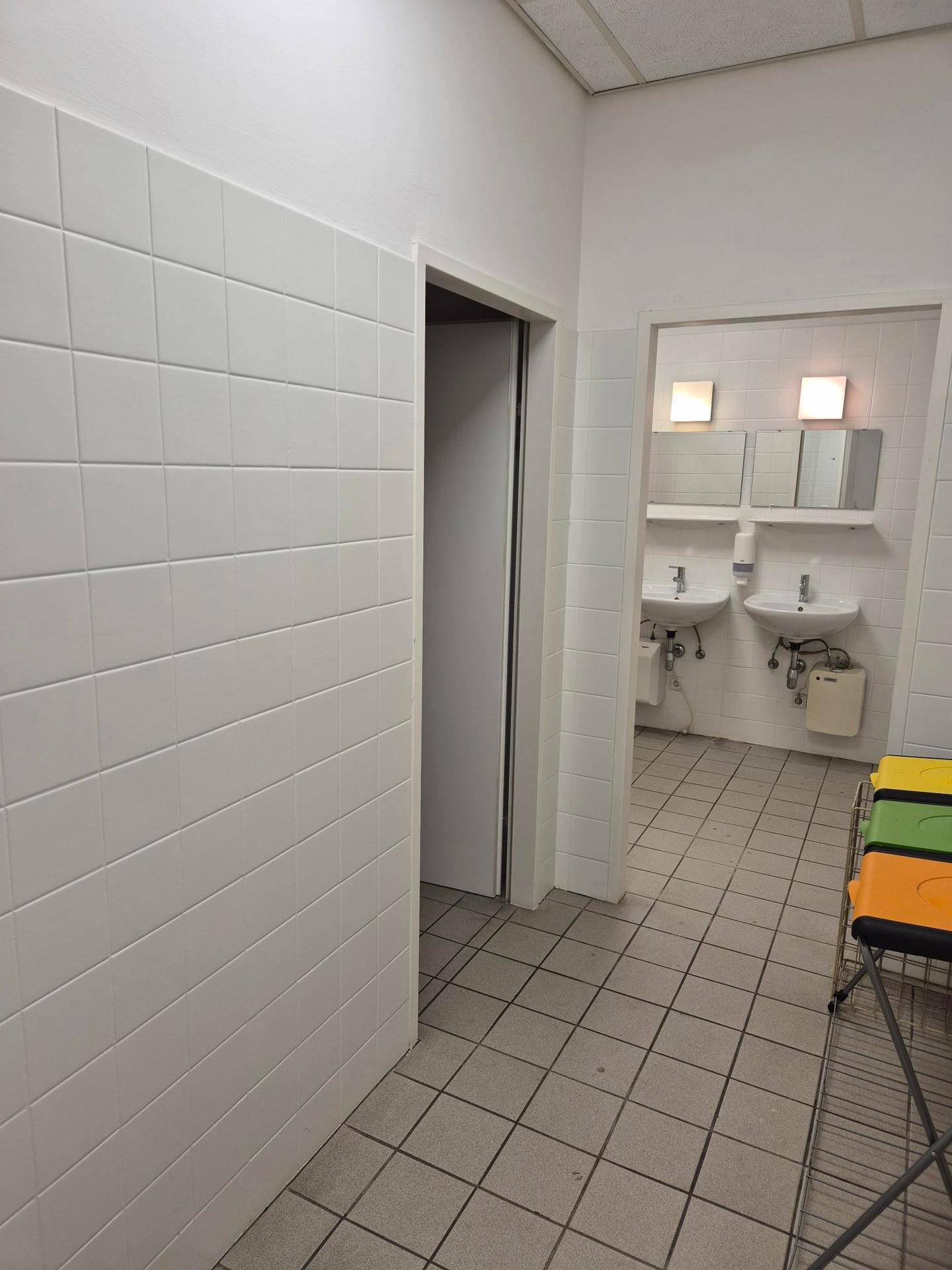 Waschraum mit zwei Waschbecken, Spiegeln und weißen Fliesen an den Wänden.