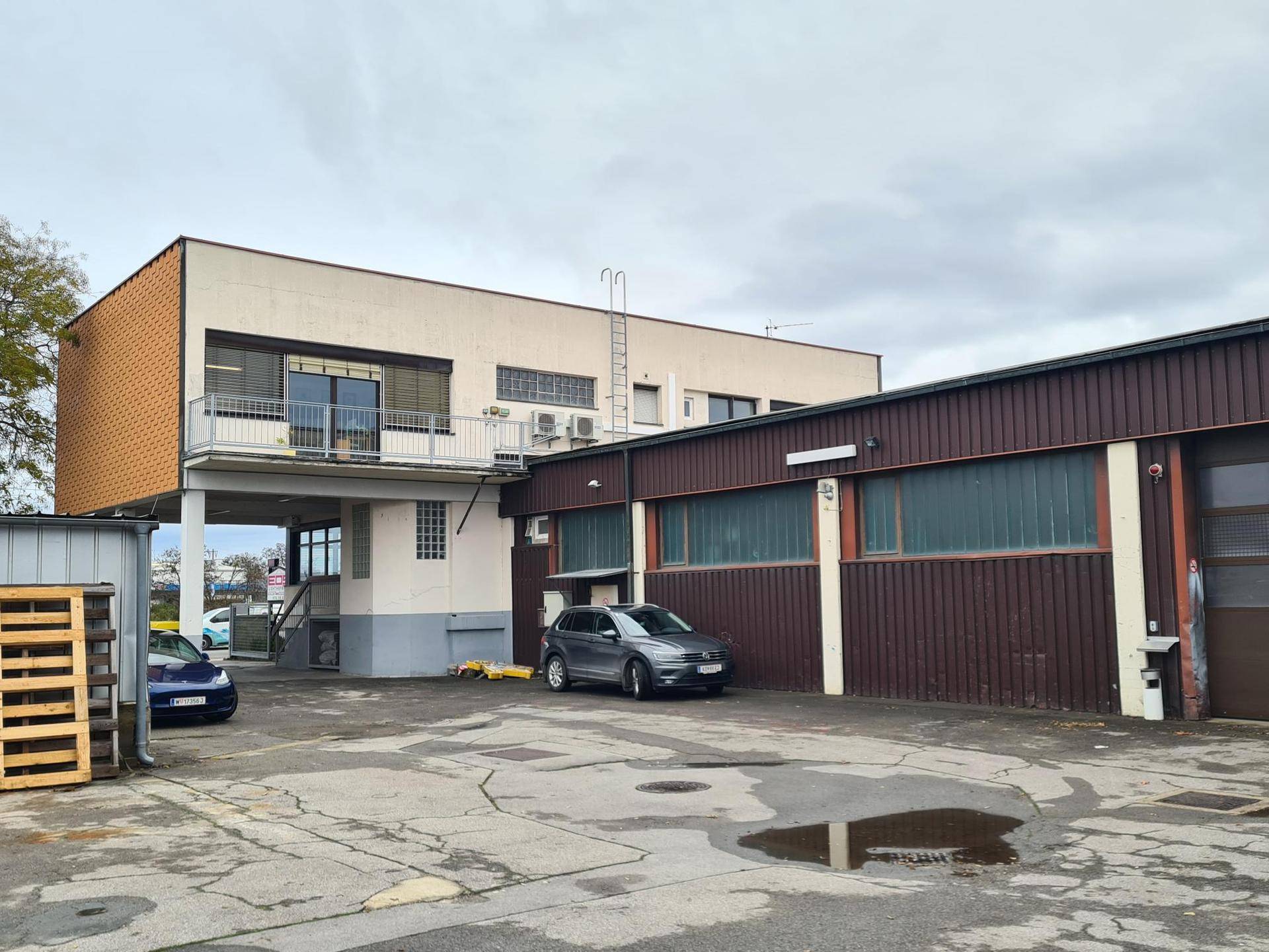 Rückansicht des Gebäudekomplexes mit Hauptgebäude, Balkon und dem braunen Wellblechgebäude.