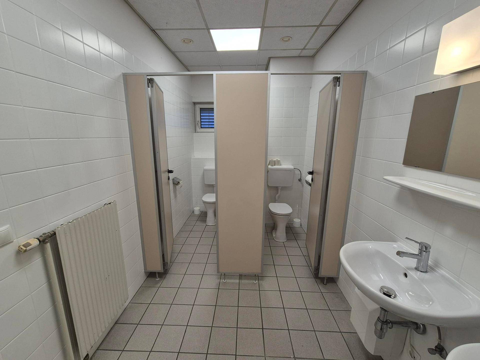 Sauberer Sanitärbereich mit Toilettenkabinen, Waschbecken und Fliesenboden.