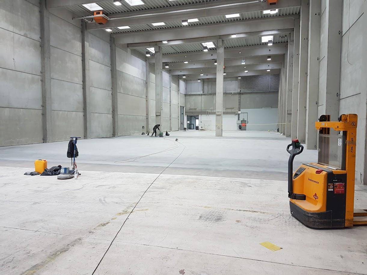 Weitläufige Lagerhalle mit Betonboden, hohen Decken und einem Gabelhubwagen im Vordergrund.