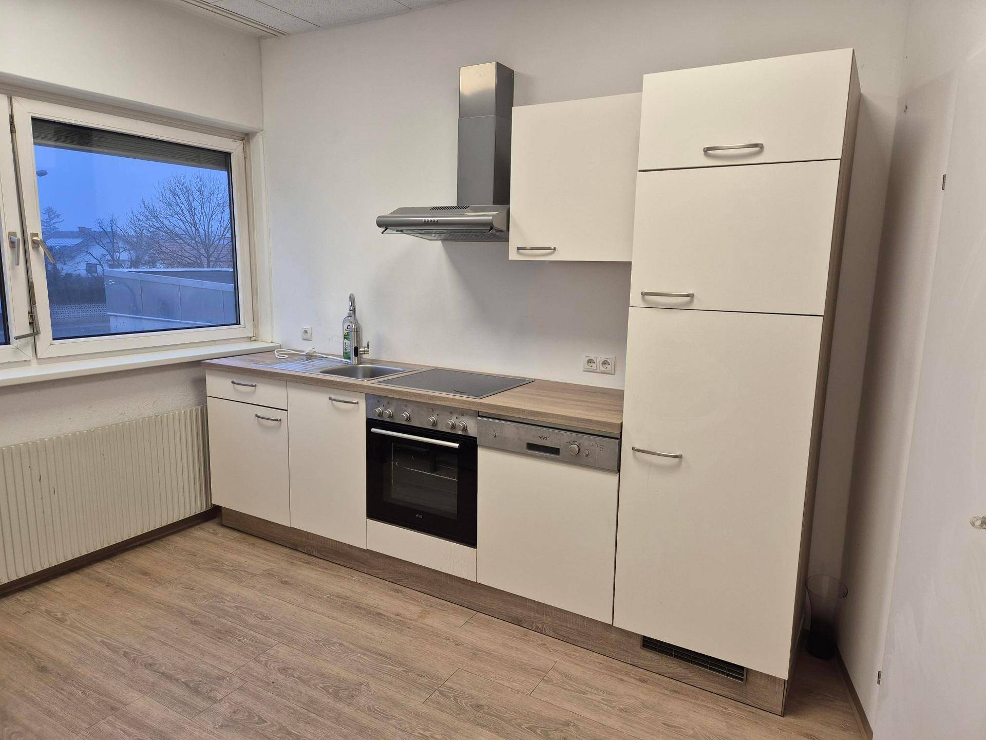 Kleine, moderne Küche mit weißen Schränken, Holzarbeitsplatte und einem Fenster mit Ausblick.