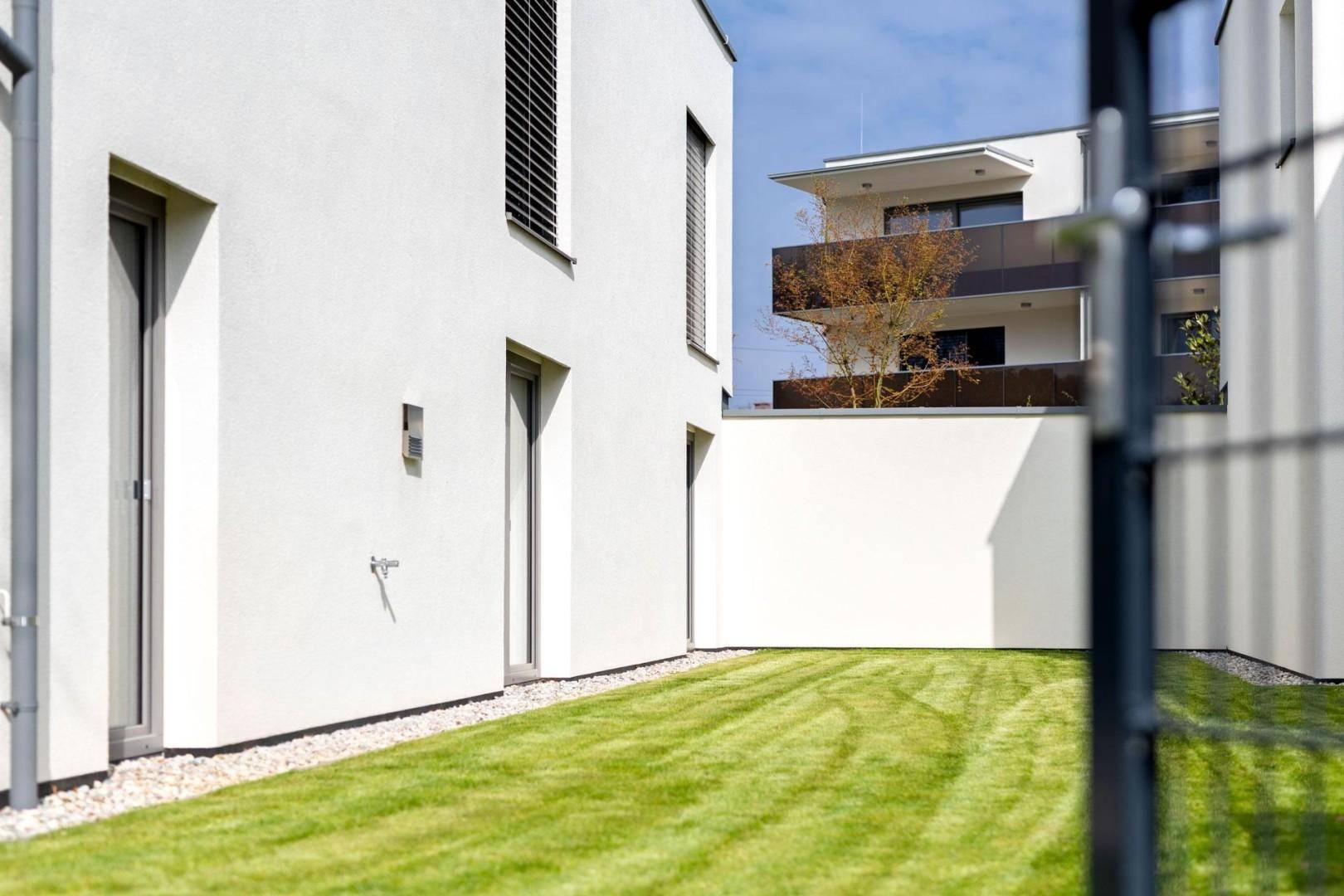 Moderner Neubau mit weißer Fassade und gepflegter Rasenfläche im Außenbereich, umgeben von weiteren Gebäuden.