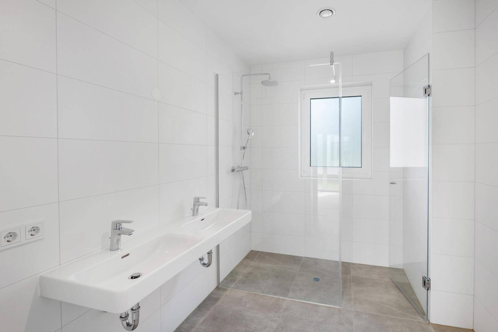 Modernes Badezimmer mit Doppelwaschbecken, großer Dusche und Fenster.
