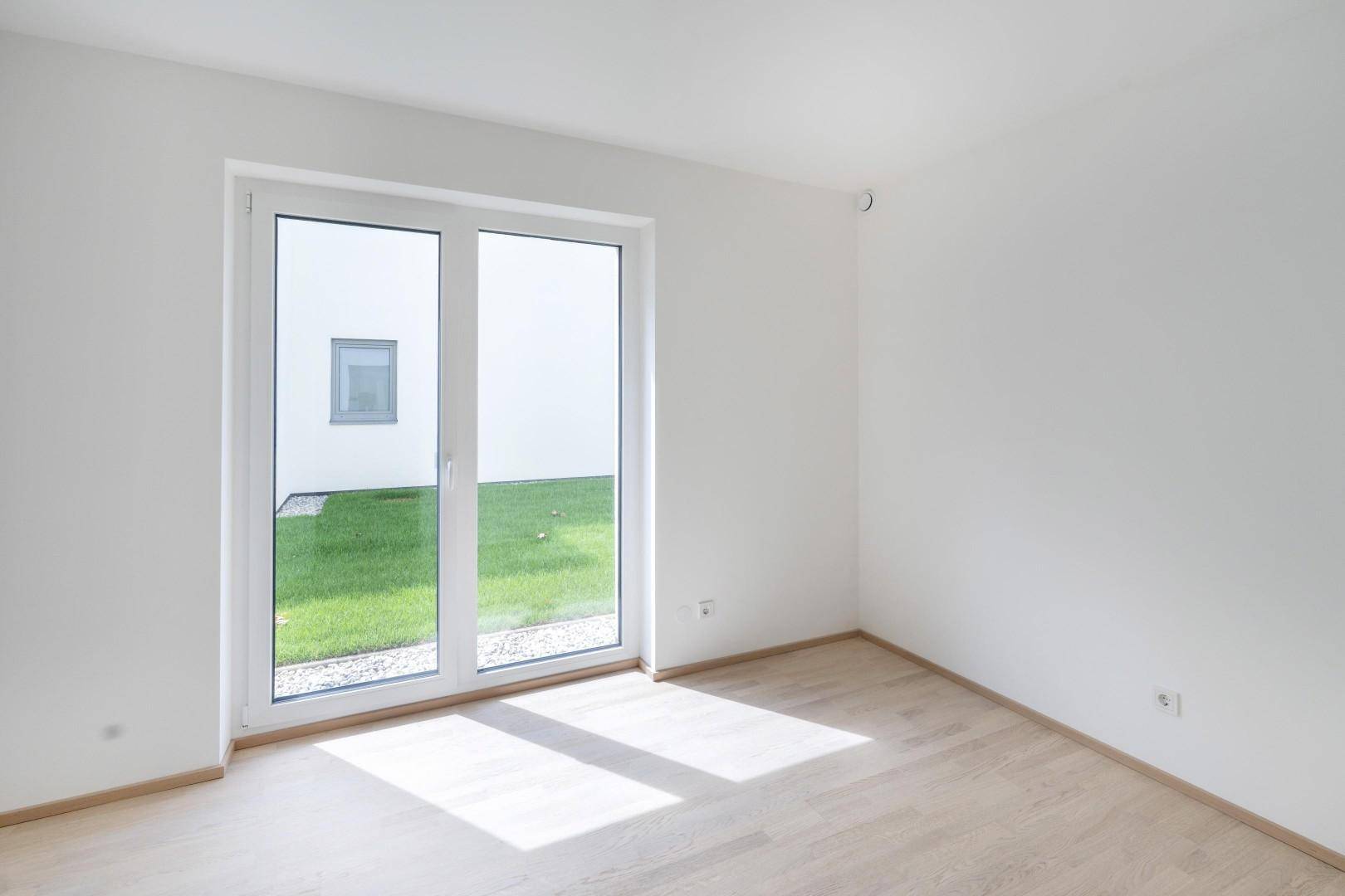 Helles Schlafzimmer mit Parkettboden und Fenster zum privaten Gartenbereich.