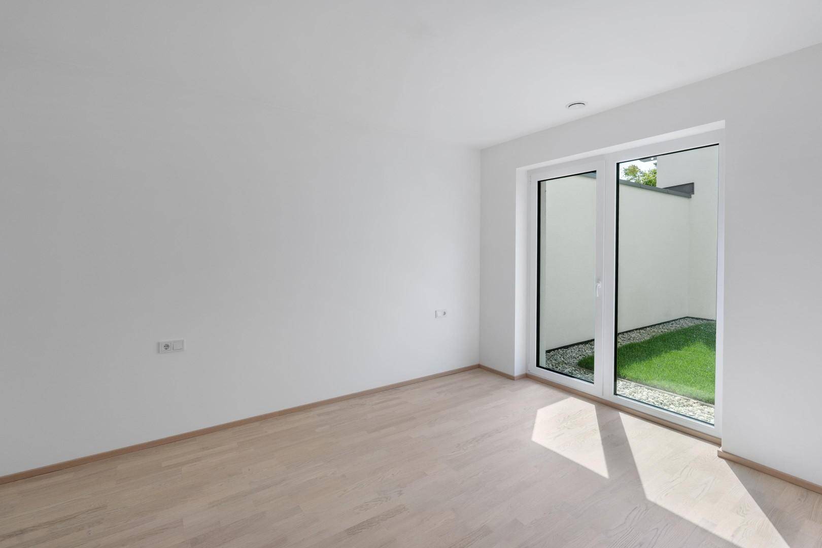Schlafzimmer mit hellem Parkettboden und Zugang zu einem kleinen Außenbereich.