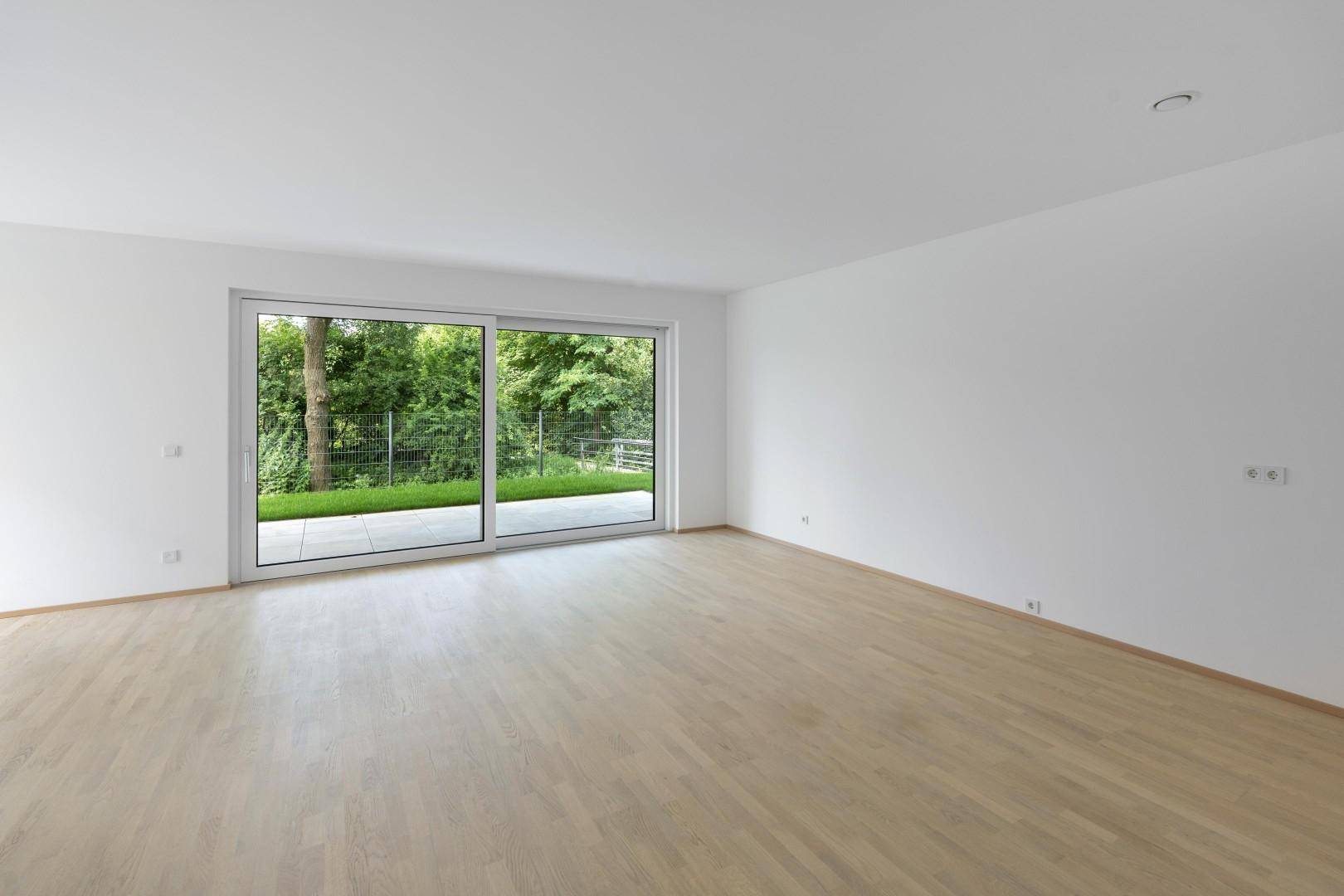 Helles Wohnzimmer mit Parkettboden und breiter Fensterfront zur Terrasse und zum Garten.