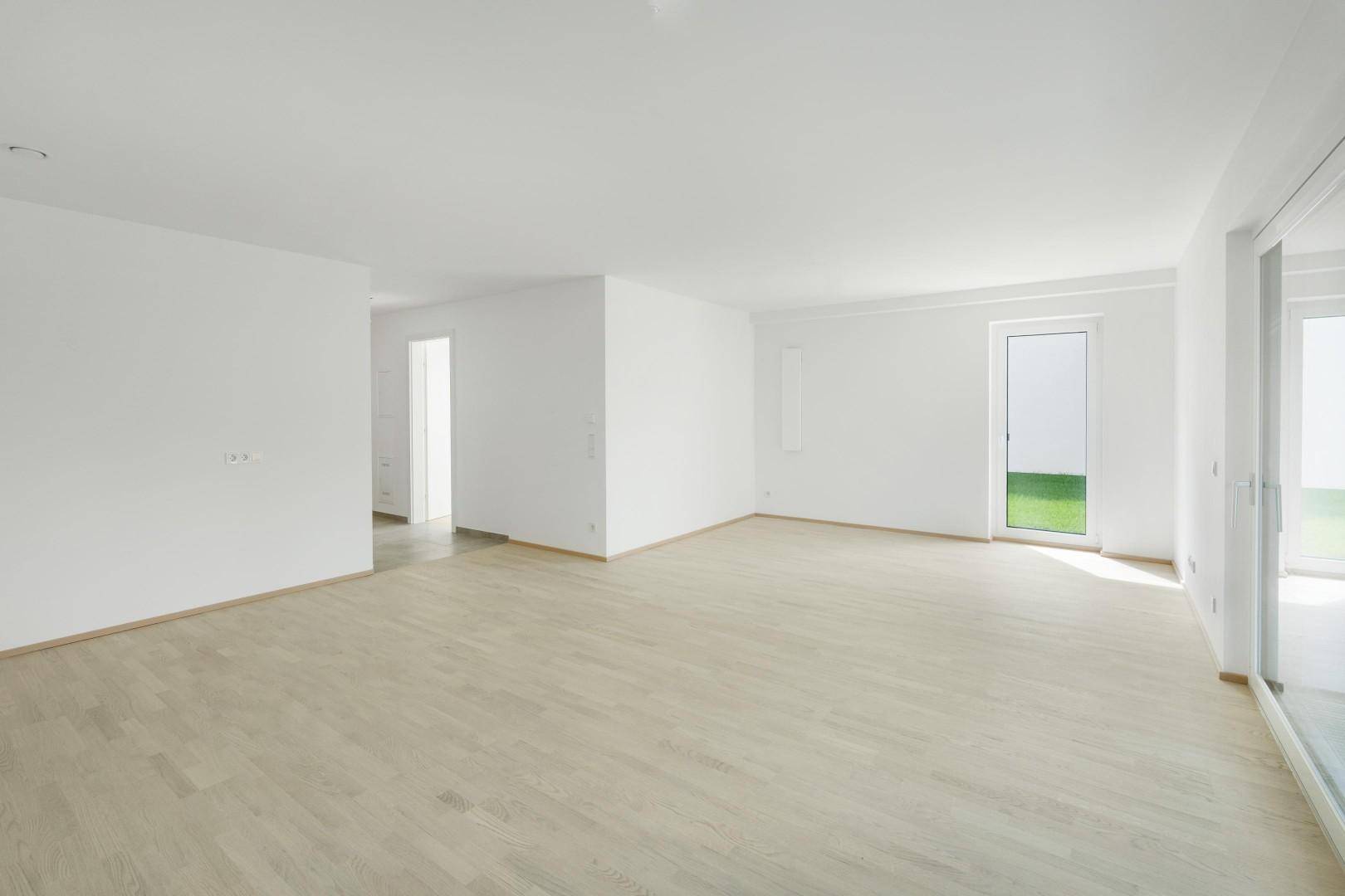 Geräumiges Wohnzimmer mit hellem Parkettboden und großen Fenstern zum Garten.