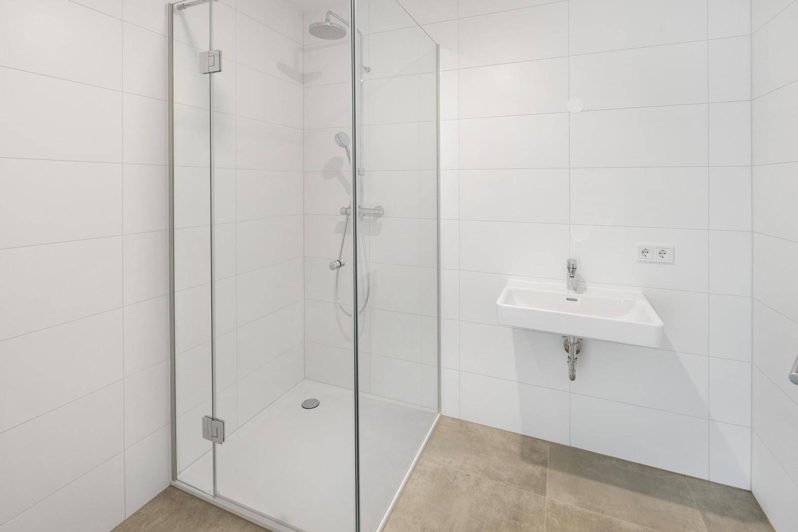 Modernes Badezimmer mit ebenerdiger Dusche, Glasabtrennung und weißem Waschbecken.