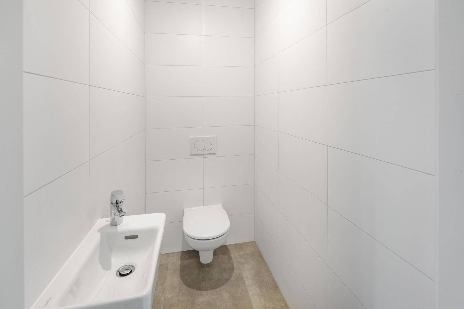 Modernes Gäste-WC mit weißen Fliesen, wandhängendem WC und kleinem Waschbecken.
