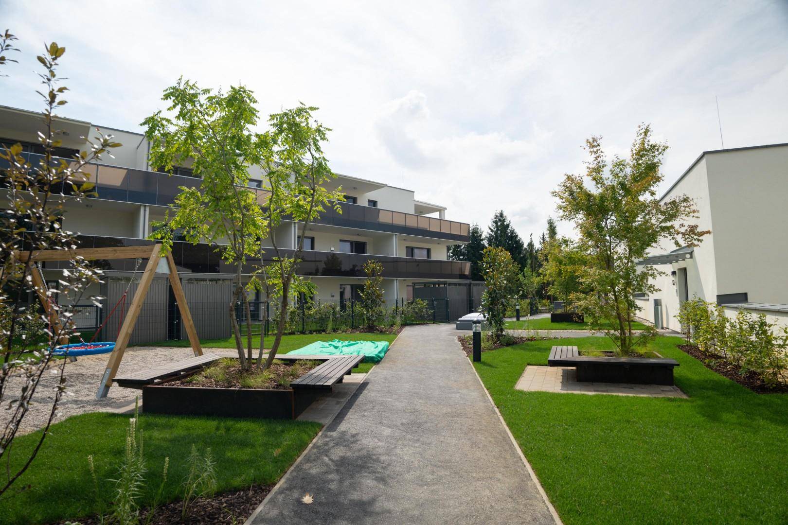 Attraktiver Gemeinschaftsbereich mit Spielplatz, Sitzgelegenheiten und Wegen zwischen den Gebäuden.