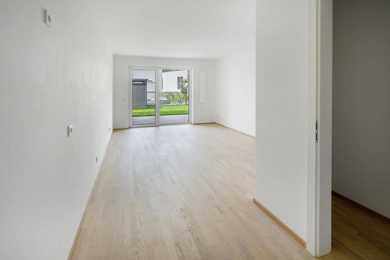 Lichtdurchflutetes Zimmer mit hellem Parkettboden und Blick auf die grüne Außenanlage.