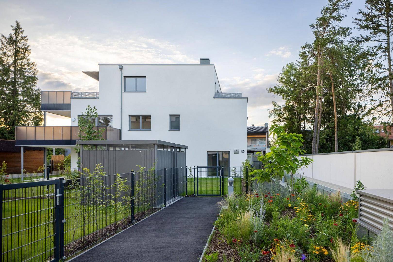 Modernes weißes Gebäude mit gepflegtem Gartenweg und grüner Bepflanzung im Außenbereich.